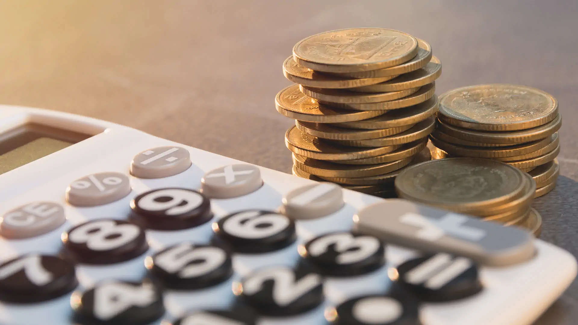 A calculator sits next to a pile of coins on a table, indicating a focus on calculations or money management.