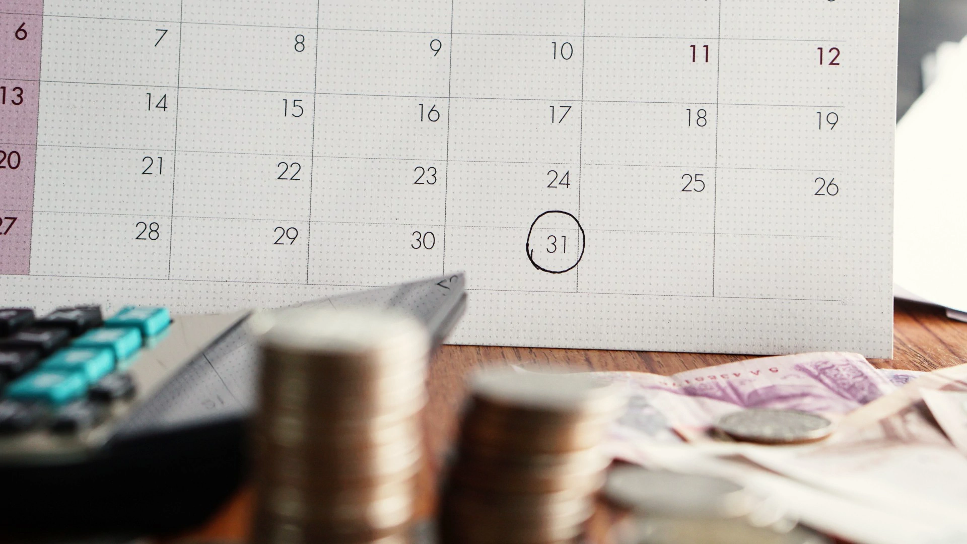 Calendar, calculator, and money arranged on a desk, suggesting financial planning or budgeting activities.