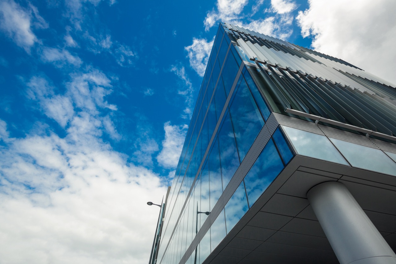 A tall office building under a vibrant blue sky filled with soft, white clouds.